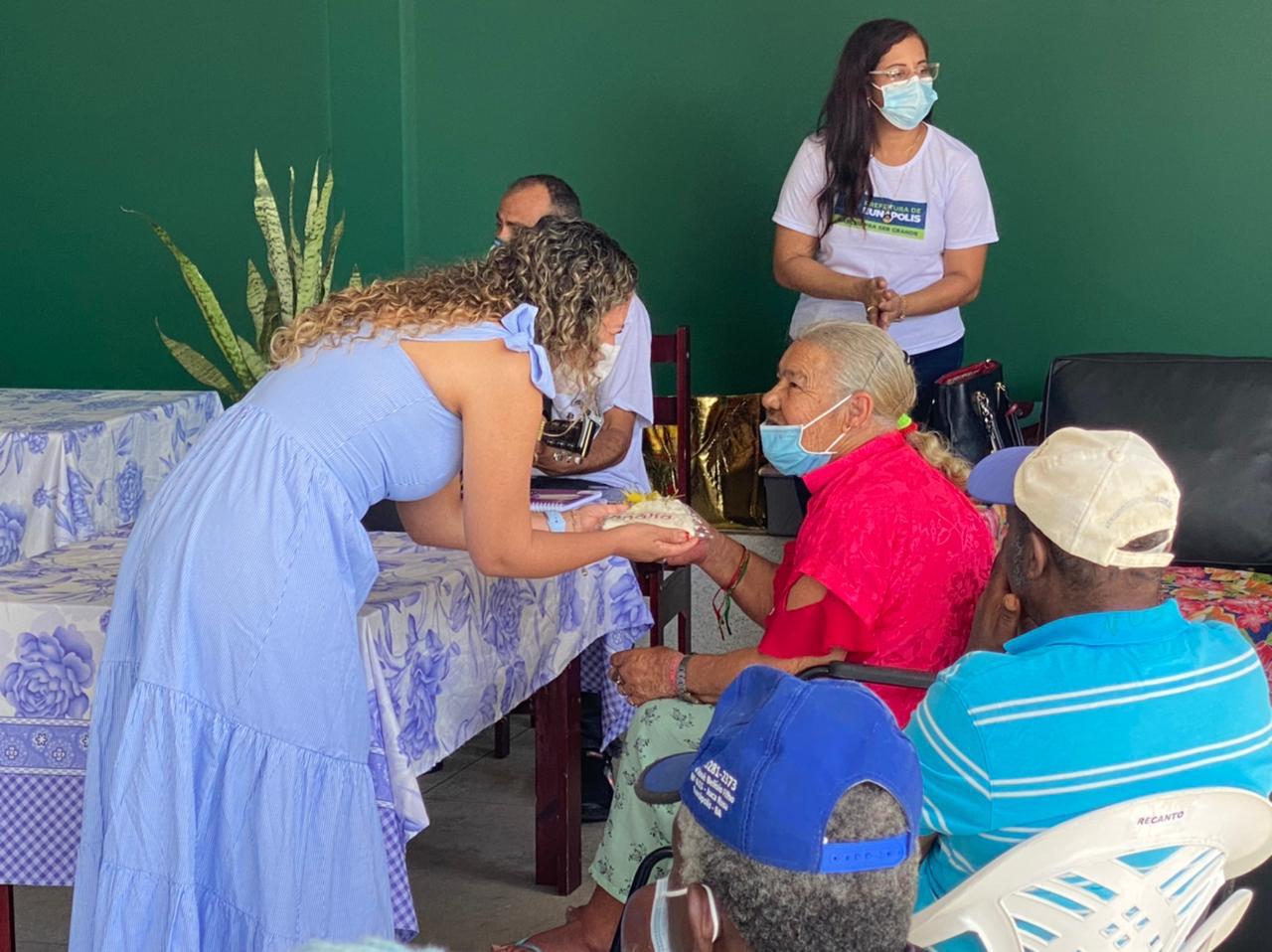 Prefeita Cordélia entrega pedaço de bolo para idosa no Dia dos Avós